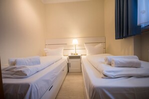 Ein Hotelzimmer mit zwei Einzelbetten, einem Nachttisch mit Lampe und einem an der Wand montierten Fernseher.