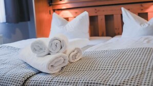 Un lit bien fait, avec des serviettes et des oreillers soigneusement pliés, une couvre-lit à carreaux et une tête de lit en bois.