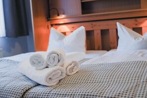 A neatly made bed with rolled towels and pillows, a checkered bedspread, and a wooden headboard.