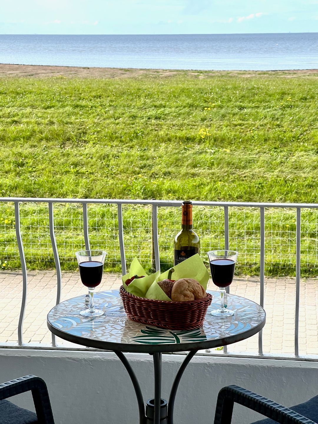 Ein Tisch mit zwei Weingläsern, einer Weinflasche und einem Brotkorb auf einem Balkon mit Blick auf ein grasbewachsenes Feld.