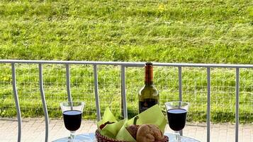 Ein Tisch mit zwei Weingläsern, einer Weinflasche und einem Brotkorb auf einem Balkon mit Blick auf ein grasbewachsenes Feld.