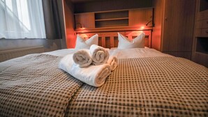 Una cama bien hecha con toallas enrolladas, una colcha a cuadros y un cabecero de madera.