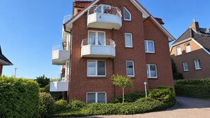 Un immeuble résidentiel à plusieurs étages, doté de balcons et d’une façade en briques, avec un ciel dégagé.