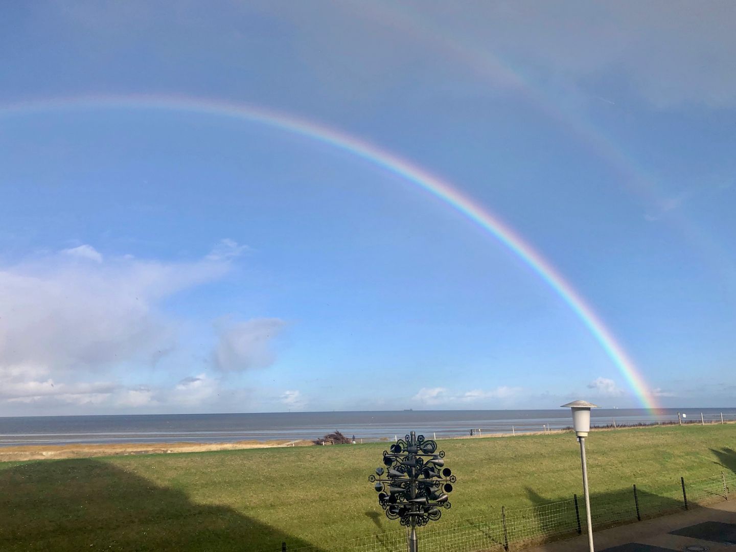 Eine begrünte Fläche mit einer Metallskulptur, einem Zaun und Blick auf das Meer.