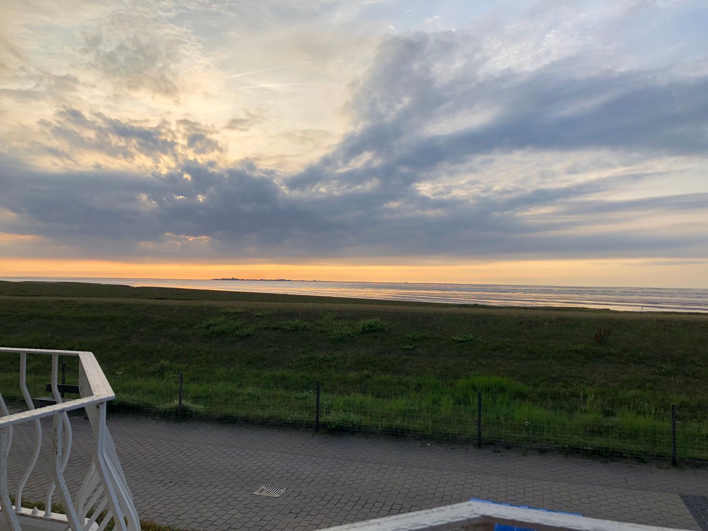 Une vue sur la plage, avec un ciel nuageux, une zone herbeuse et une promenade dallée.