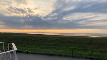 Une vue sur la plage, avec un ciel nuageux, une zone herbeuse et une promenade dallée.