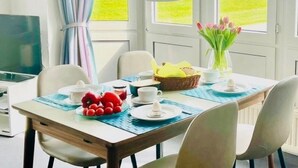 Un coin repas avec une table dressée pour deux personnes, un ordinateur portable, un panier de pain et un vase de fleurs.