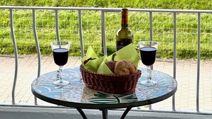 Una mesa con dos copas de vino, una botella y una cesta de pan en un balcón con vistas a un campo cubierto de hierba.