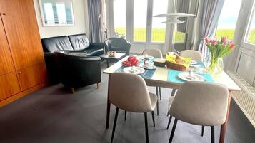 Ein Essbereich mit einem für zwei Personen gedeckten Tisch, einer schwarzen Ledersofa und Blick ins Freie.