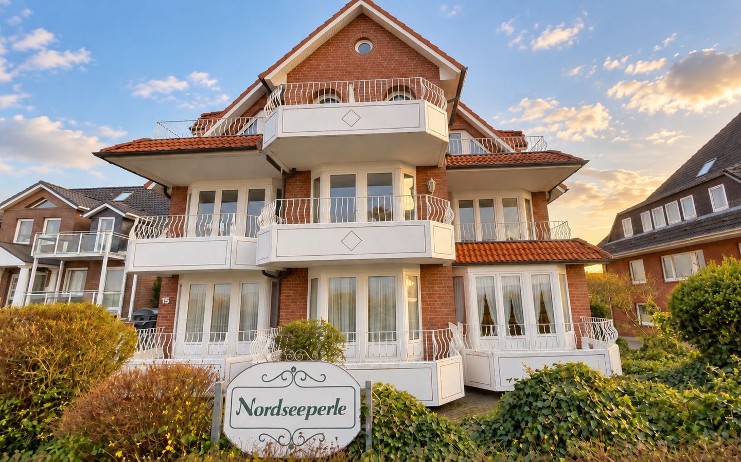 Ein mehrstöckiges Gebäude mit Balkonen, einem Schild mit der Aufschrift 'Nordseeperle' und einer Ziegel-Fassade.