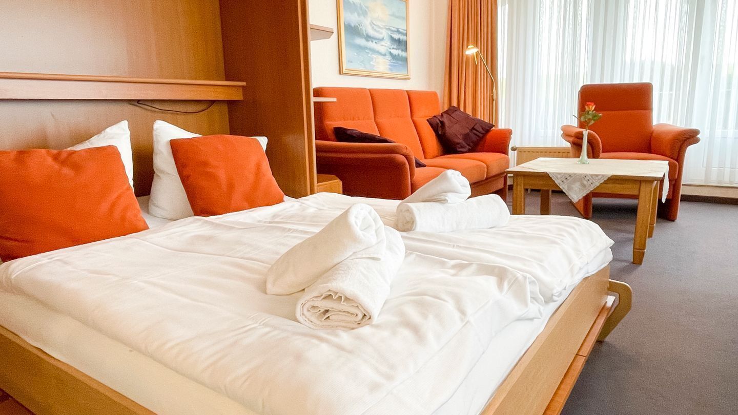 Ein Hotelzimmer mit einem Bett, zwei orangefarbenen Sesseln, einem kleinen Tisch und einem Gemälde an der Wand.