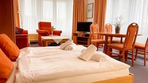 A hotel room with a bed, orange chairs, a TV, and a table with a plant. - Nordseeperle Whg 4 - Ihre Ferienwohnung für 4 Personen - Haus Nordseeperle (Cuxhaven)