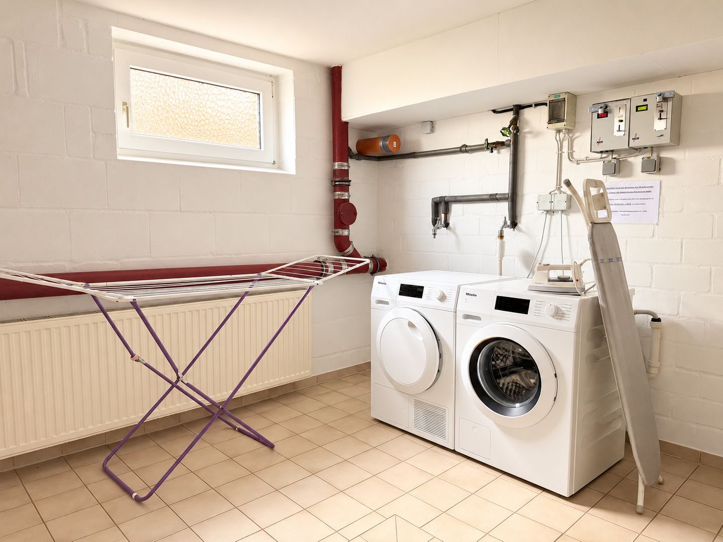 Une buanderie équipée d’un étendoir, de deux machines à laver, d’un radiateur et d’une fenêtre.