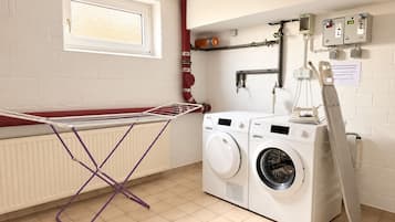 Une buanderie équipée d’un étendoir, de deux machines à laver, d’un radiateur et d’une fenêtre.