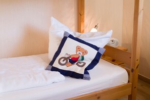 Ein Bett mit weißer Matratze, einem Kopfkissen mit einem Bärenmotiv und einem Holzkopfstück.