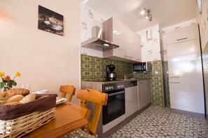 Une cuisine compacte équipée d’une cuisinière, d’un four, d’un four à micro-ondes et d’un réfrigérateur. On y trouve une table à manger avec des chaises et un vase de fleurs.