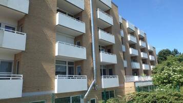 Ein mehrgeschossiges Wohngebäude mit Balkonen, einer Ziegel-Fassade und einem grünen Zaun.