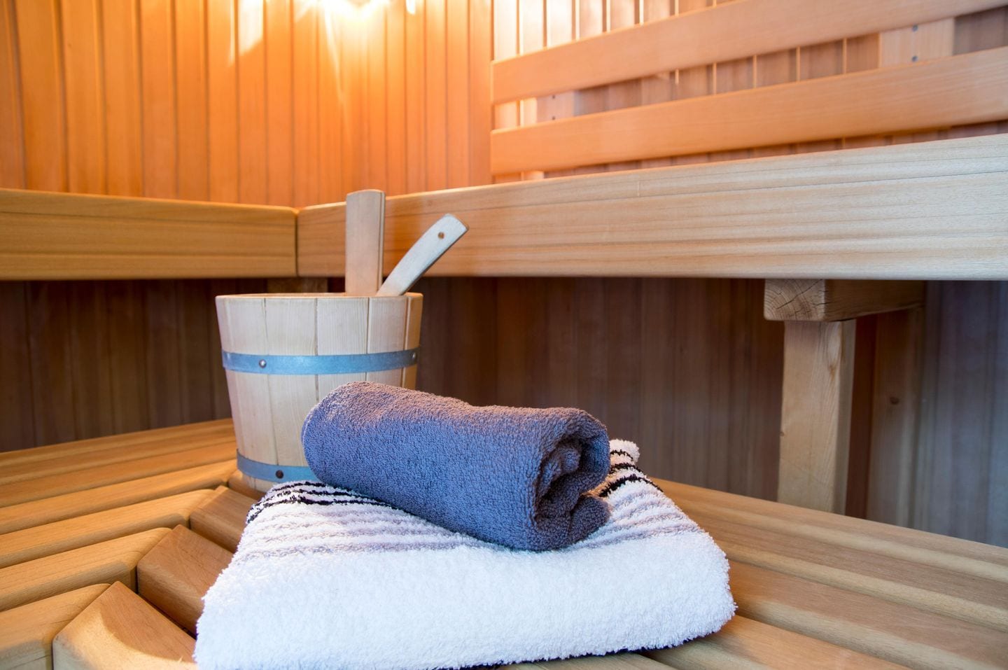 A sauna with wooden benches, a towel, and a wooden bucket with a brush.