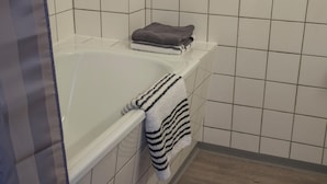Un baño con una bañera blanca, un perchero con una toalla doblada y paredes de azulejos.