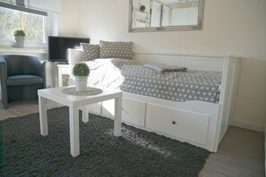 A bedroom with a bed, a small table, a chair, a TV, and a window with a plant. - FP61 studio for 2 people with modern facilities and swimming pool & sauna in the (Cuxhaven)