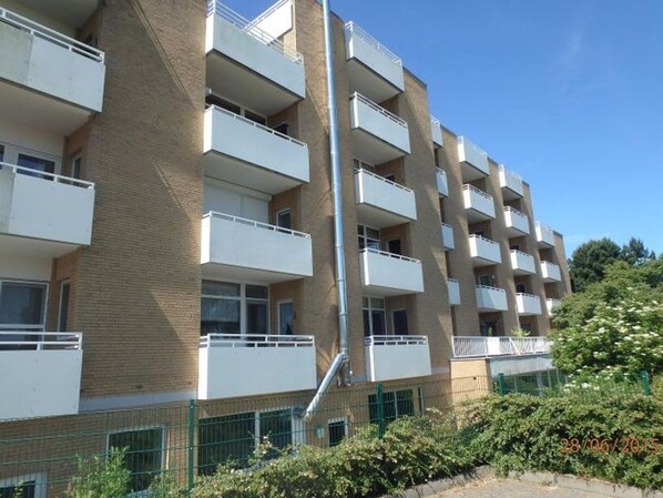 Un edificio residencial de varios pisos con balcones, fachada de ladrillo y valla verde.