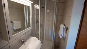 Un baño moderno con ducha de vidrio, un lavabo blanco y un espejo con una toalla colgada en la pared.