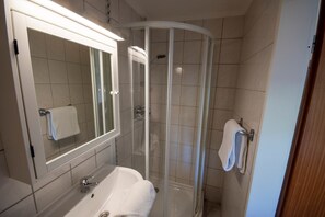 Un baño moderno con ducha de vidrio, un lavabo blanco y un espejo con una toalla colgada en la pared.
