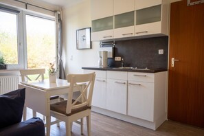 Una cocina compacta con armarios blancos, encimera negra y ventana con cortinas.