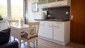 Une cuisine de taille réduite avec des meubles blancs, un plan de travail noir et une fenêtre agrémentée de rideaux.