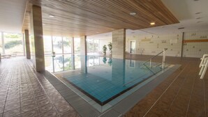 Une piscine intérieure avec des parois en verre transparent, un plafond en bois et des carreaux de sol à motifs.