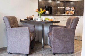 A modern kitchen with a dining table, two upholstered chairs, a coffee maker, and a coffee machine.