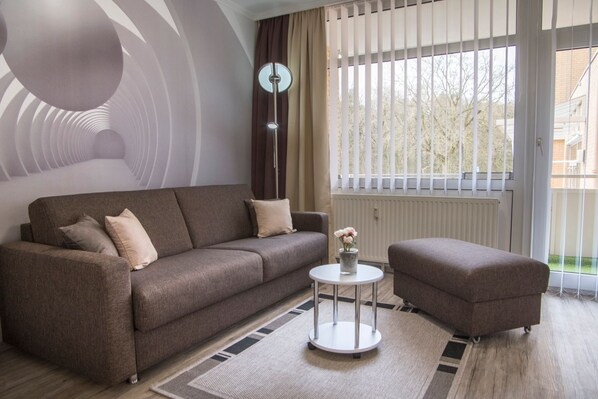 A modern living room with a sofa, ottoman, and a small table with flowers.