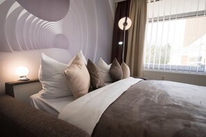 A modern bedroom with a bed, pillows, a nightstand, and a lamp.