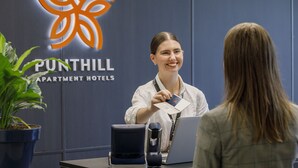 A hotel reception desk with a logo, a plant, and a laptop. - Punthill Essendon North (Essendon)