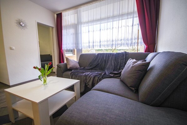 A living room with a gray sofa, a small white table, and a vase with flowers.
