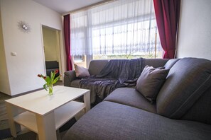 Una sala de estar con un sofá gris, una mesita blanca y un florero con flores.