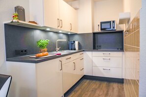 Una cocina moderna con armarios blancos, encimera negra, microondas y una planta pequeña.