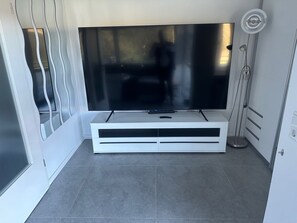 A modern living room with a flat-screen TV on a white entertainment unit, grey tiled flooring, and a minimalist design.