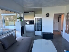 Un salon moderne avec un canapé, une table basse en verre et une cuisine en arrière-plan.