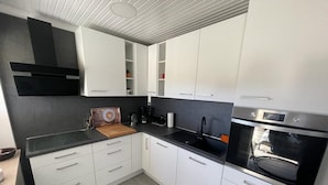 Moderni keittiö, jossa on valkoiset kaapit, musta työtaso ja sisäänrakennettu uuni.
