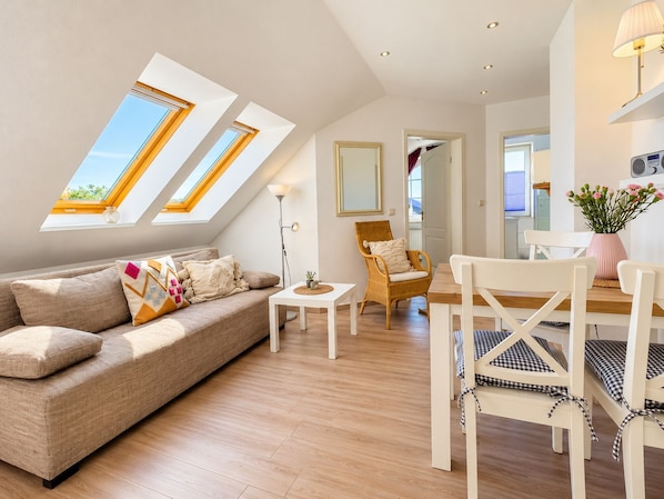 A modern living room with a sofa, a dining table, and a chair. There are skylights on the ceiling.