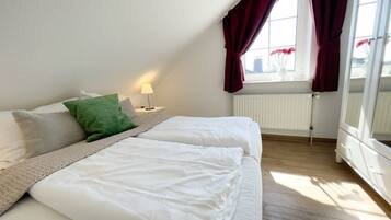 Ein Schlafzimmer mit zwei Betten, einem Heizkörper, einem Fenster mit Vorhängen und einem Nachttisch mit Lampe.