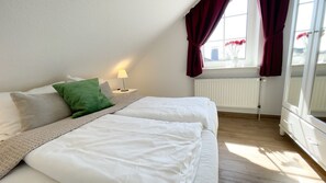 Un dormitorio con dos camas, un radiador, una ventana con cortinas y una mesita de noche con lámpara.
