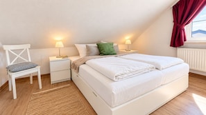 A bedroom with a bed, nightstands, a chair, and a window with curtains.