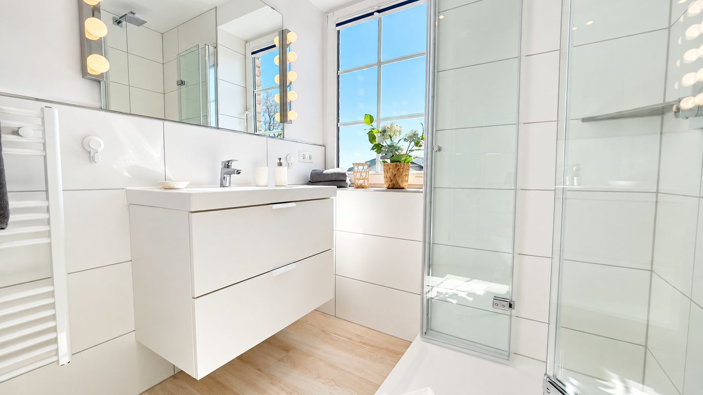 A modern bathroom with a white vanity, a glass shower enclosure, and a large window providing natural light.
