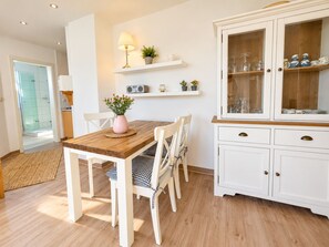 Een eethoek met een houten tafel en stoelen, een kast met glazen deuren en een radio op een plank.