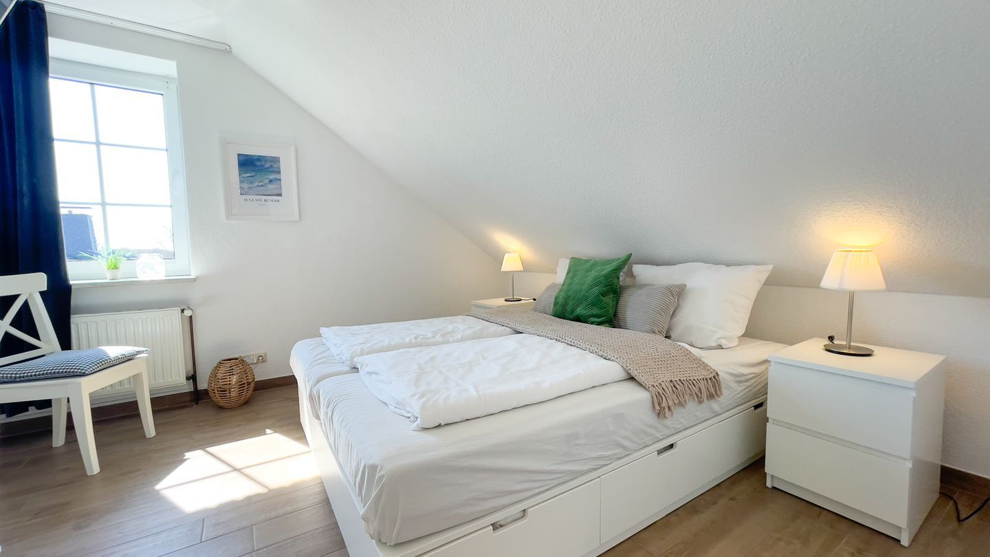 Ein Schlafzimmer mit einem Bett, Nachttischen, einem Sessel und einem Fenster.