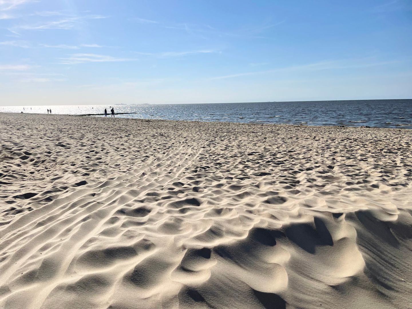 Ein Sandstrand mit sanften Wellen und blauem Himmel.