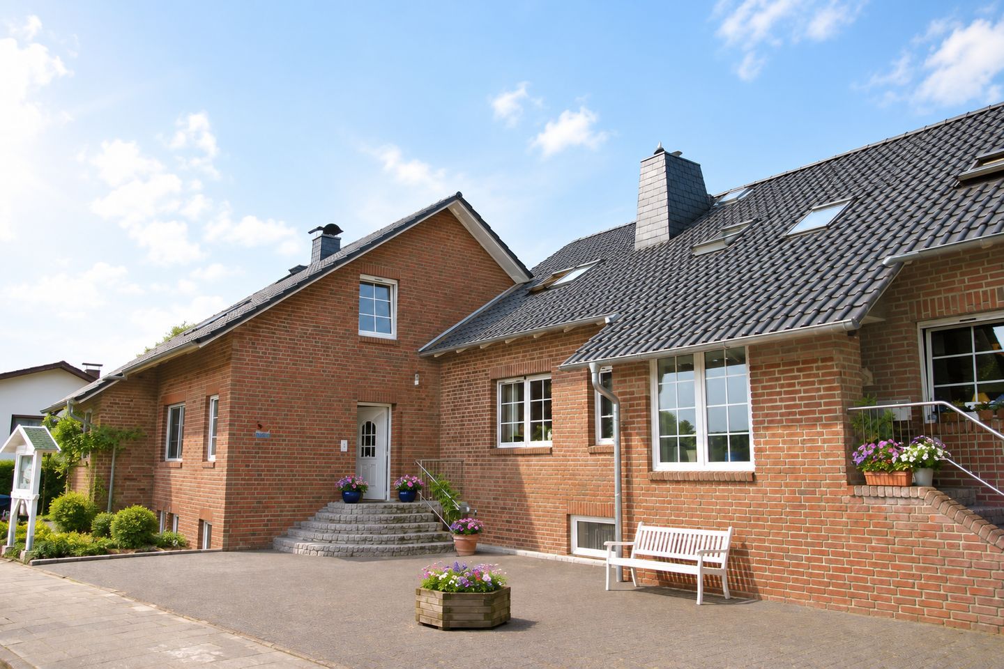 Et tosset rødstenshus med en veranda, skorsten og en lille have med krukkeplanter.