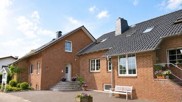 Et tosset rødstenshus med en veranda, skorsten og en lille have med krukkeplanter.